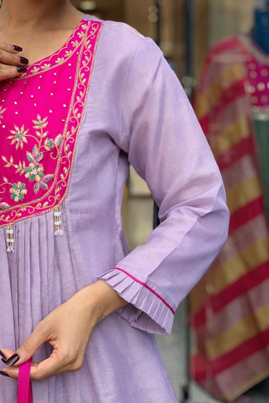 Elegant lavender kurta set with a striking magenta yoke, detailed floral embroidery, fine zari work, and pearl tassels for a rich festive look.
